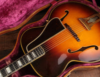 Close-up of a vintage acoustic guitar in a case with a purple interior.