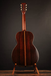Back view of an acoustic guitar on a stand against a dark background