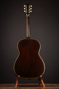 1947 Gibson LG-2 acoustic guitar with a sunburst finish on a stand against a dark background, back view