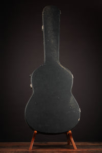 Vintage Gibson acoustic guitar case on a stand against a dark background