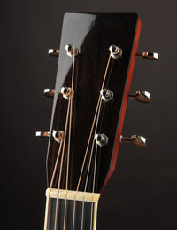 Close-up of a guitar headstock with tuning pegs on a dark background