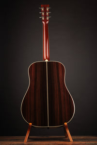 Acoustic guitar on a stand against a black background, back view