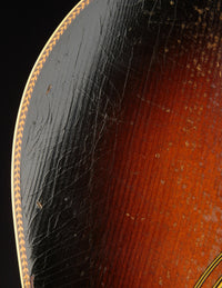 Close-up of a guitar's top with a dark brown and red color gradient.