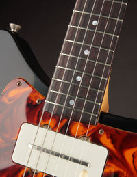 Close-up of a guitar with tortoiseshell pickguard and white pickup.