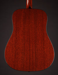 Acoustic guitar with a natural wood finish on a black background, back view