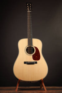 Front view of a Collings acoustic guitar on a stand against a dark background