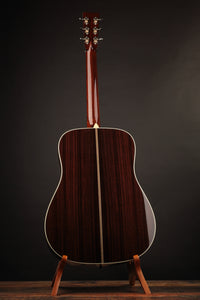 Back view of a Collings acoustic guitar on a stand against a dark background