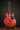 Red electric guitar on a stand against a dark background