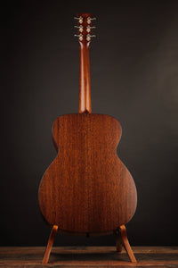 Acoustic guitar on a stand against a dark background, back view.