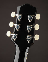 Close-up of a guitar headstock with tuning pegs on a dark background