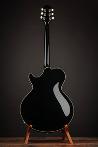 Black electric guitar on a stand against a dark background