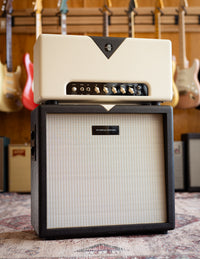 Guitar amplifier head and cab with guitars in the background