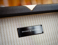 Close up of Divided by Thirteen speaker cabinet with guitars in the background