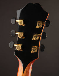 Close-up of a guitar headstock with tuning pegs on a dark background