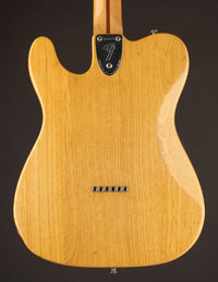 Back view of a Fender electric guitar with a natural wood finish on a black background