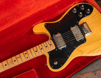Electric guitar with a wooden body and neck, placed inside a red lined case.