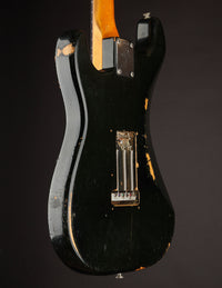 Back view of a black 1968 Fender Stratocaster electric guitar with visible wear on a dark background