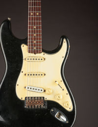 Black 1968 Fender Stratocaster electric guitar with a white pickguard on a dark background, close up