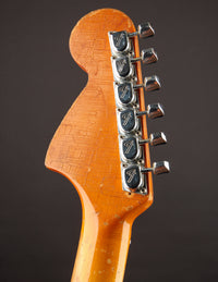 Close-up of a guitar headstock with tuning pegs on a dark background