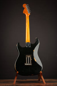 Black 1968 Fender Stratocaster on a stand against a dark background, back view 