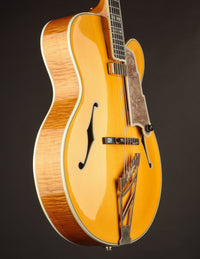 Side view of a blonde archtop guitar on a dark background