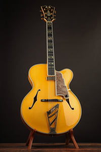 Blonde archtop guitar on a stand against a dark background