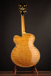 Back view of a blonde archtop guitar on a stand against a dark background