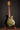 Guitar with black body and gold pickguard on a stand against a dark background