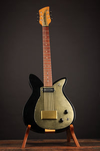 Guitar with black body and gold pickguard on a stand against a dark background