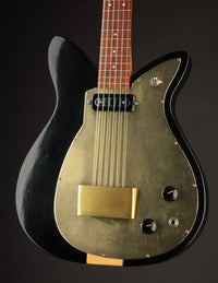 Glossy black electric guitar with gold pickguard on a dark background