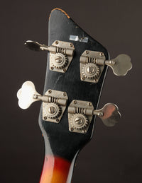Close-up of a bass guitar headstock with tuning pegs on a dark background