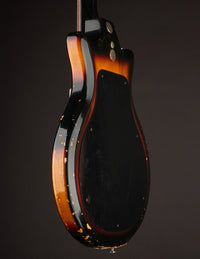 Close-up of a bass guitar body with a dark brown and black finish on a dark background