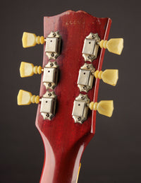 Close-up of a red guitar headstock with tuning pegs on a dark background