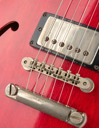 Close-up of a red electric guitar with a focus on the bridge and strings.