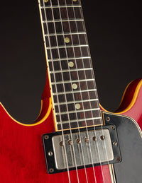 Close-up of a red electric guitar with a black pickguard on a dark background