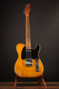 Telecaster guitar with a blonde finish on a stand against a dark background
