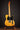 Electric guitar with a natural finish on a stand against a black background