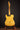 Blonde electric guitar on a stand against a dark background