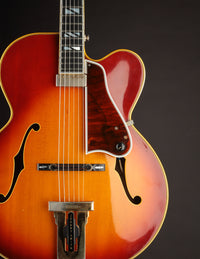 Close up of a vintage Johnny Smith archtop guitar with a sunburst finish on a dark background