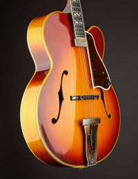 Side view of a vintage Johnny Smith archtop guitar with a sunburst finish on a dark background