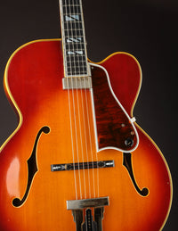 Close up of a vintage Johnny Smith archtop guitar with a sunburst finish on a dark background