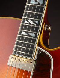Close up of fingerboard and neck pickup on a vintage Johnny Smith archtop guitar with a sunburst finish on a dark background
