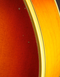 Close up of binding on a vintage Johnny Smith archtop guitar with a sunburst finish on a dark background