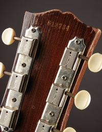 Close-up of a guitar headstock with tuning pegs and brand name on a dark background
