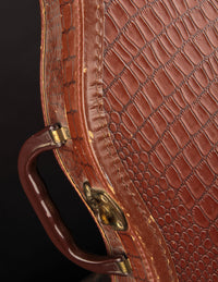 Close-up of a brown textured vintage guitar case with gold hardware on a dark background
