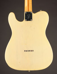Back view of a Fender electric guitar with a blonde finish on a dark background