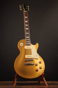 Gold electric guitar on a stand against a dark background