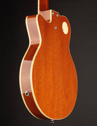 Brown electric guitar with a white pickguard on a dark background, back/side view