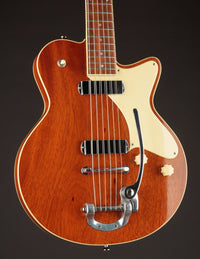 Brown electric guitar with a white pickguard on a dark background