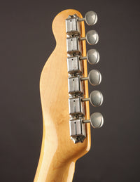 Close-up of a telecaster headstock with tuning pegs on a dark background